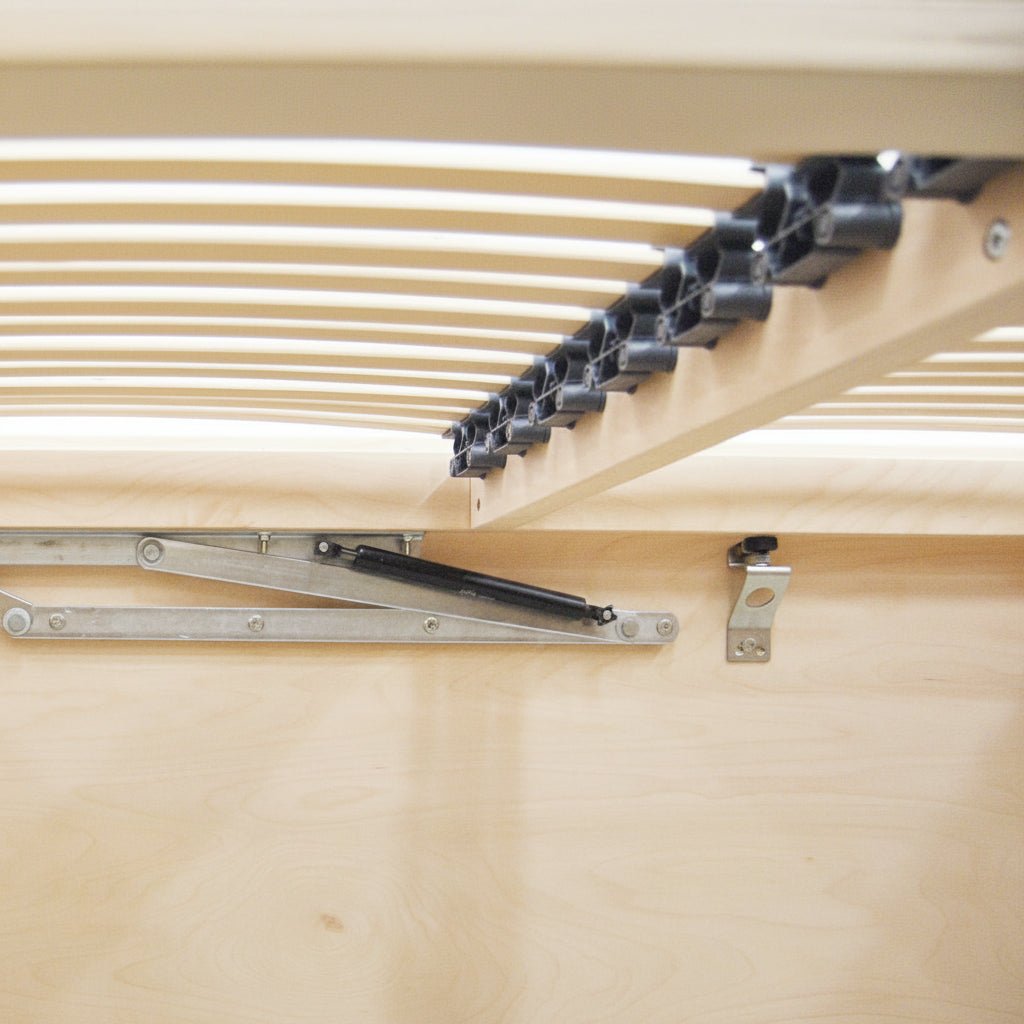 Close-up of a wooden slatted bed frame underside with metal support brackets and a light-colored floor.
